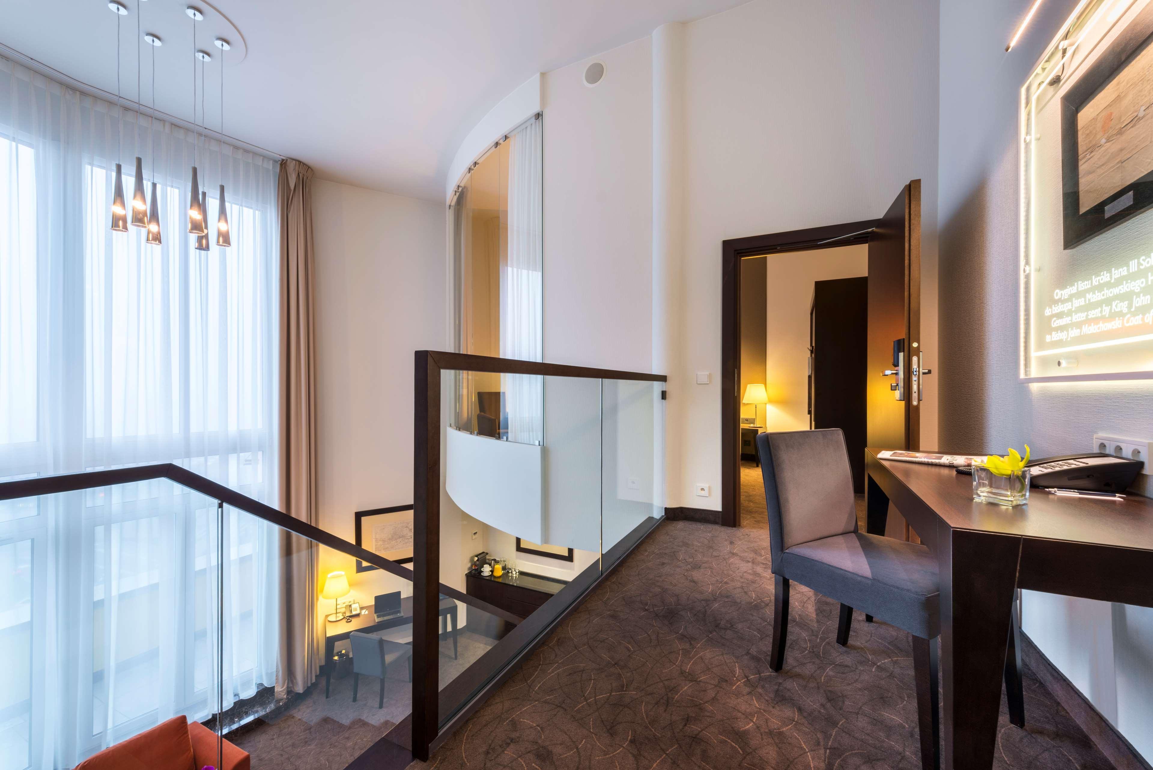 Radisson Blu Sobieski Warsaw Exterior photo The photo depicts a modern interior space, likely a hotel suite or a stylish apartment. There is a staircase leading to an upper level, with a glass railing providing an open atmosphere. The lighting is bright, coming from large windows adorned with 